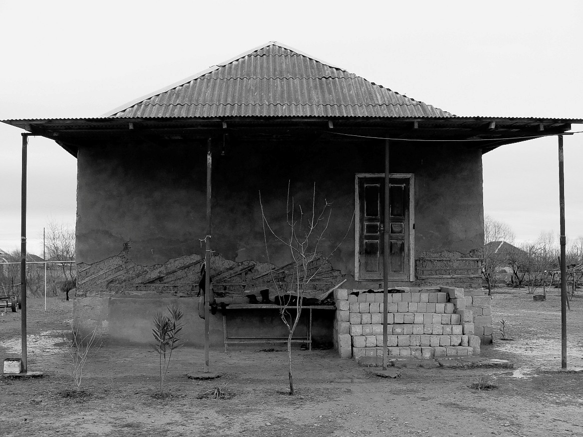 Home in Sabirabad. Two years ago a major flood ravaged the area. The water damage clearly exposes the underlying wood, mortar, and plaster where the water level reached. The government has promised to build them a new home, but right now all that stands is a dirt mound for the foundation.