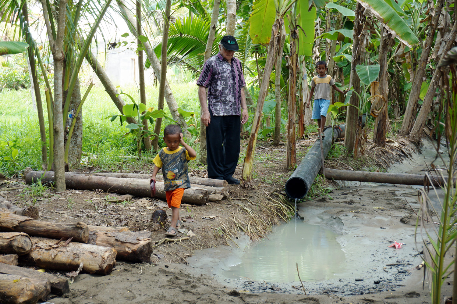 Father Charlie and kids watching the pumped water come out of the pipe. Photo credit: Yungkit