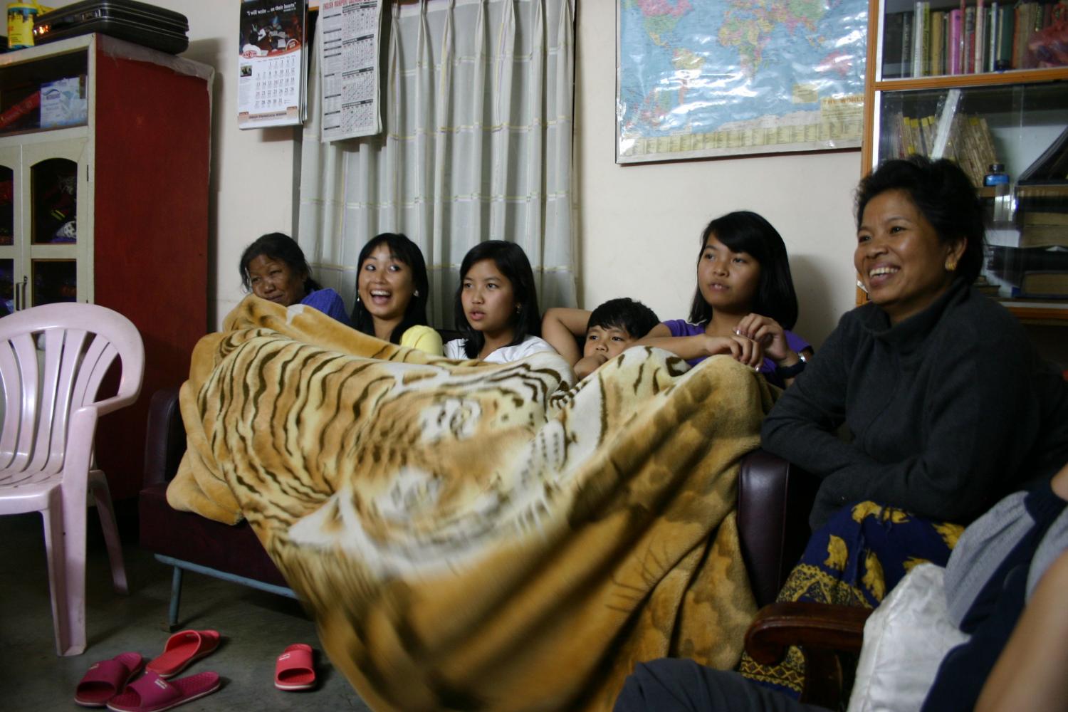 After a long day of enjoying the festival, a family watches the "Miss Kut" competition from their T.V. at home.